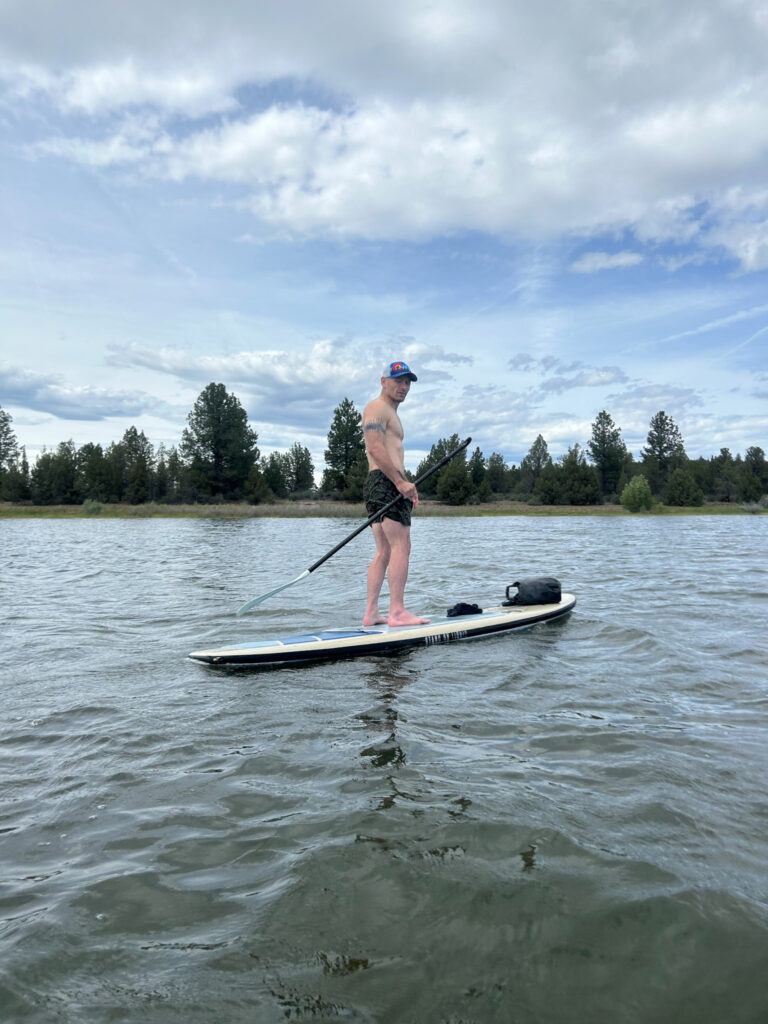 A man standing paddle boarding shirtless on the reservoir.  