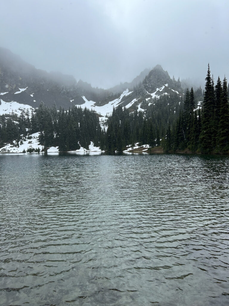 A beautiful lake with snow coming down and fog covering the mountains