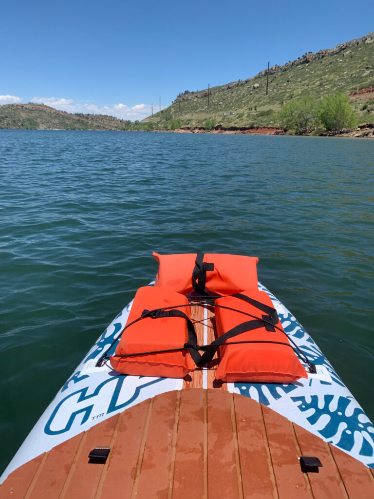 A view of the front of a paddle board in the water with Horsetooth reservoir as the back drop. 