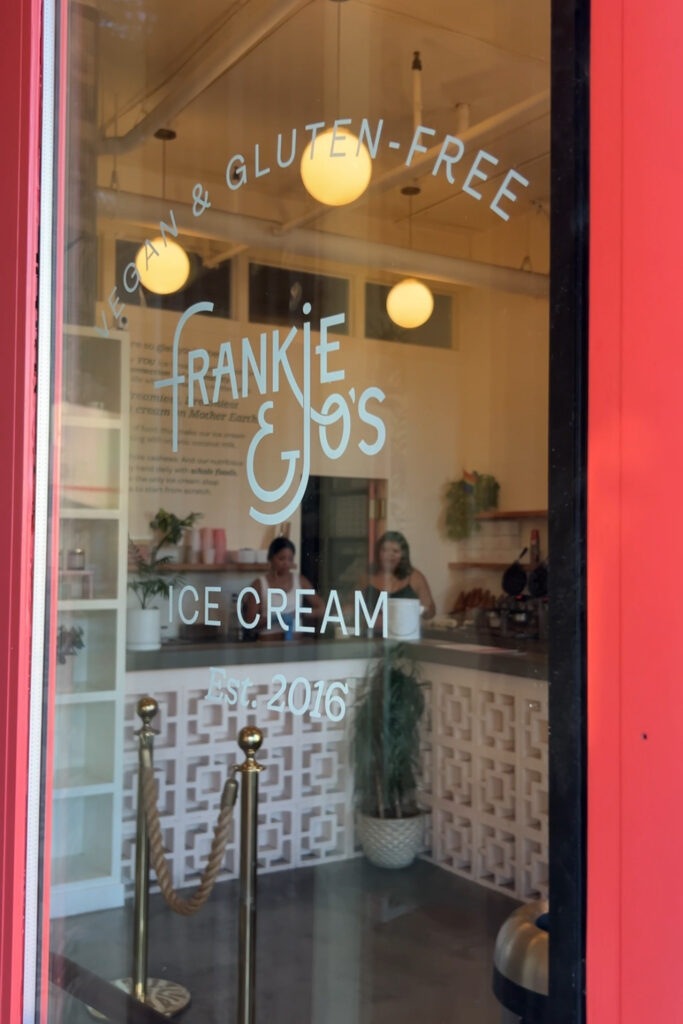 A see through door with the name frankie & Joes in white text. You can see through to the ice cream shop inside.