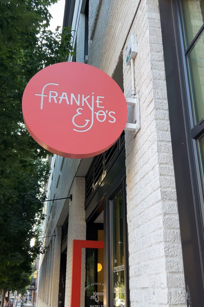 A pink sign that says Frankie & Joes on the outside of a building. This is the name of the ice cream shop.